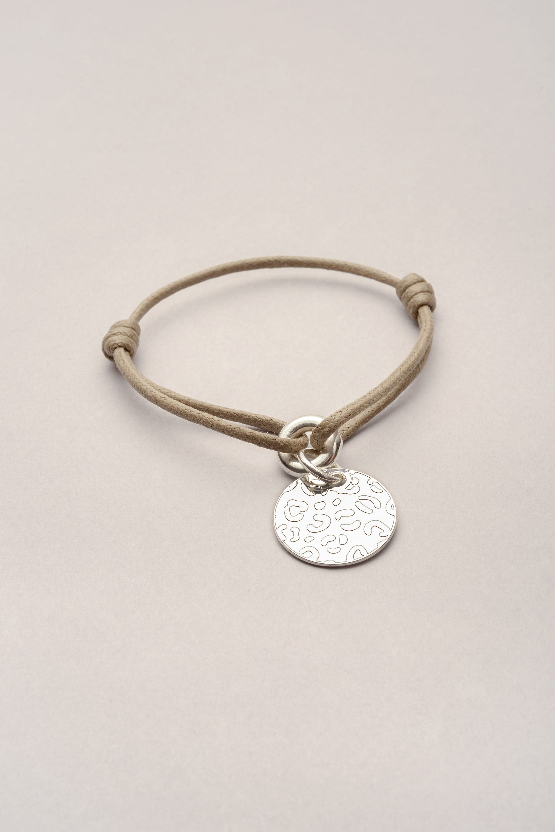 Ce bracelet est composé d'un cordon coloré réglable et d'une médaille ronde avec des reliefs léopard. Bijou fantaisie ajustable avec deux noeuds coulissants. 