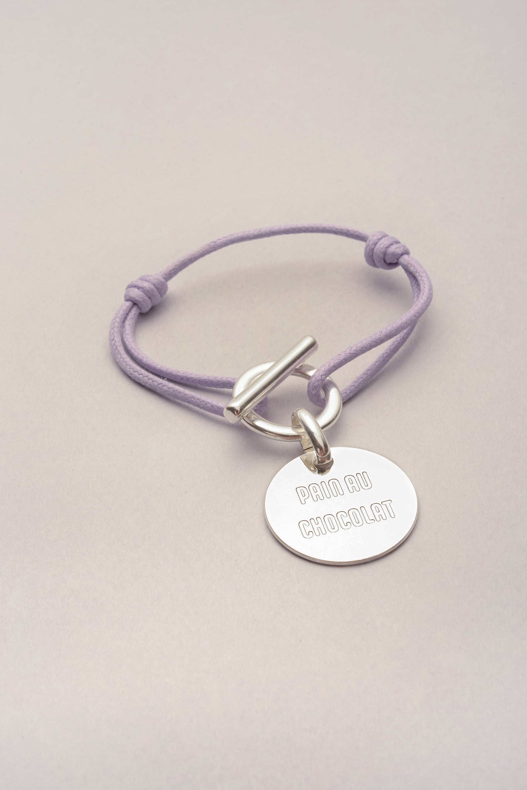 Bracelet attache medaille Pain au Chocolat avec cordon de coton colore, existe aussi en version chocolatine. Ce bijou se compose d'un cordon et d'un fermoir en T. 