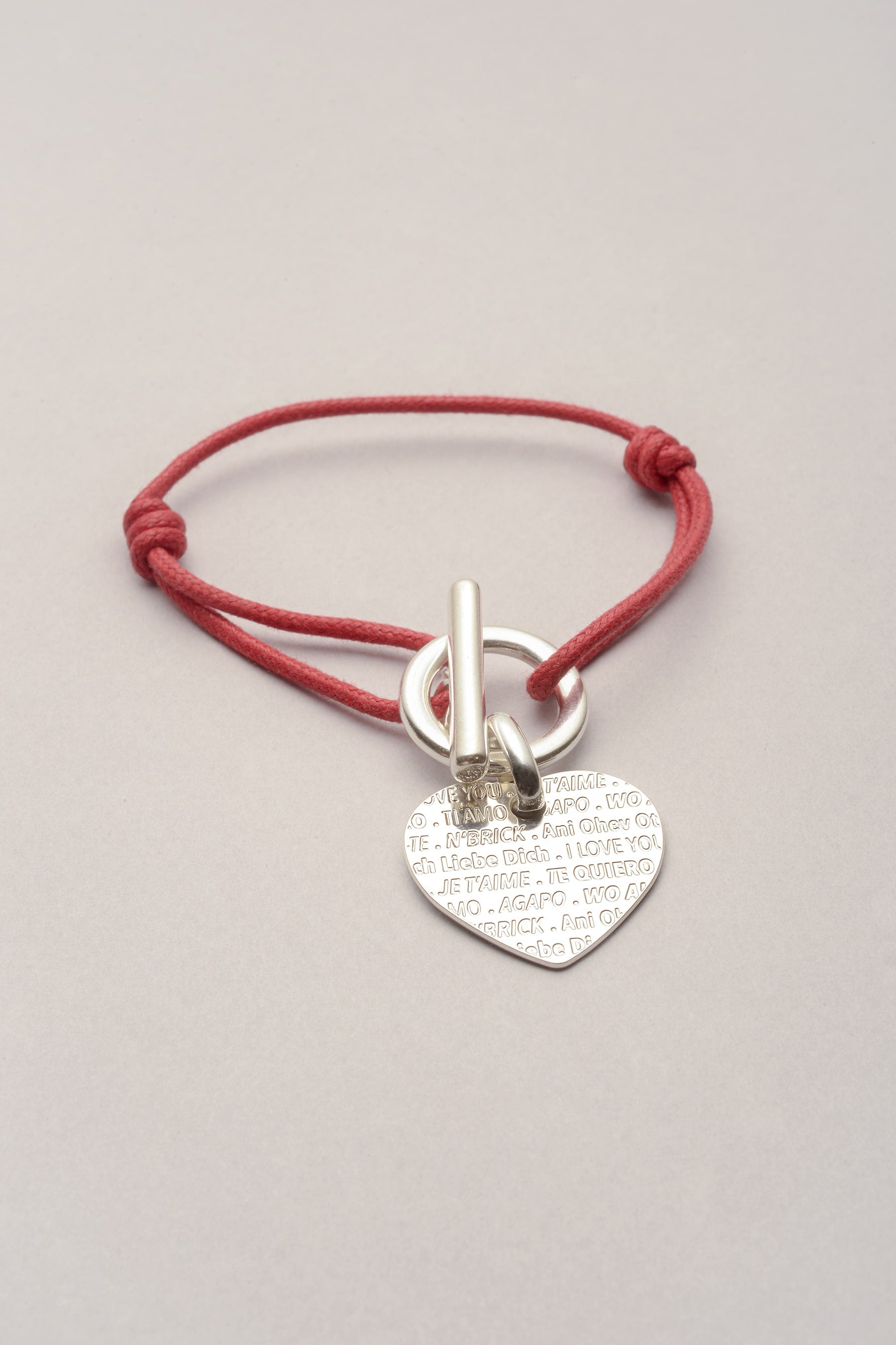 Bracelet argenté avec cordon de coton coloré et pendentif en forme de coeur. Sur le coeur on peut les la phrase je t'aime en plusieurs langues, inspiré du mur des je t'aime à Paris. Le bracelet s'ouvre et se ferme grâce à un fermoir en T. 