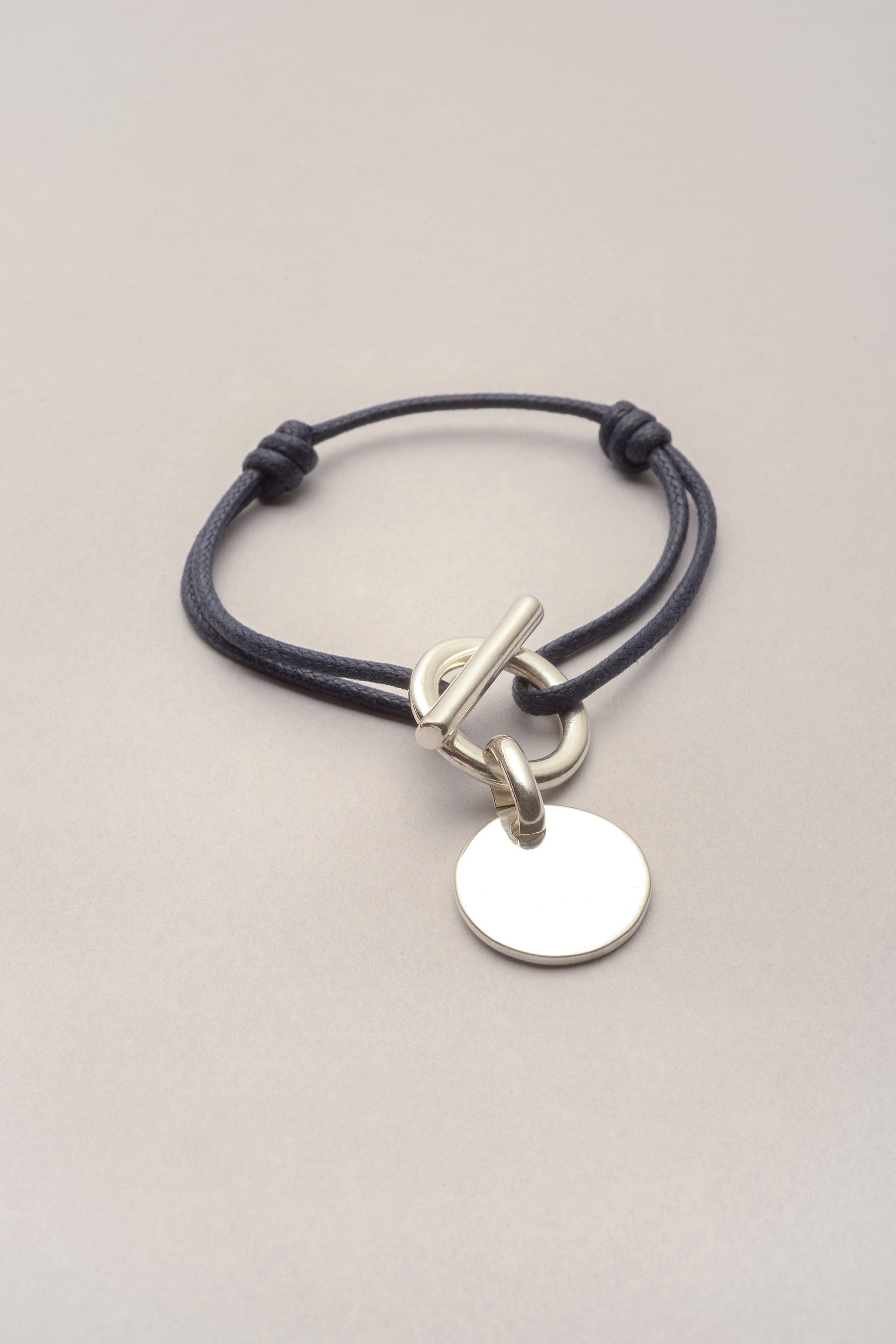 Ce bracelet se compose d'un cordon de coton coloré et d'une attache. Sur l'attache, il y a une médaille de 20mm classique et lisse. L'attache est un fermoir en T, ce qui rend pratique l'utilisation de ce bracelet. Ce bijou est idéal pour commencer sa première collection de bracelets. 