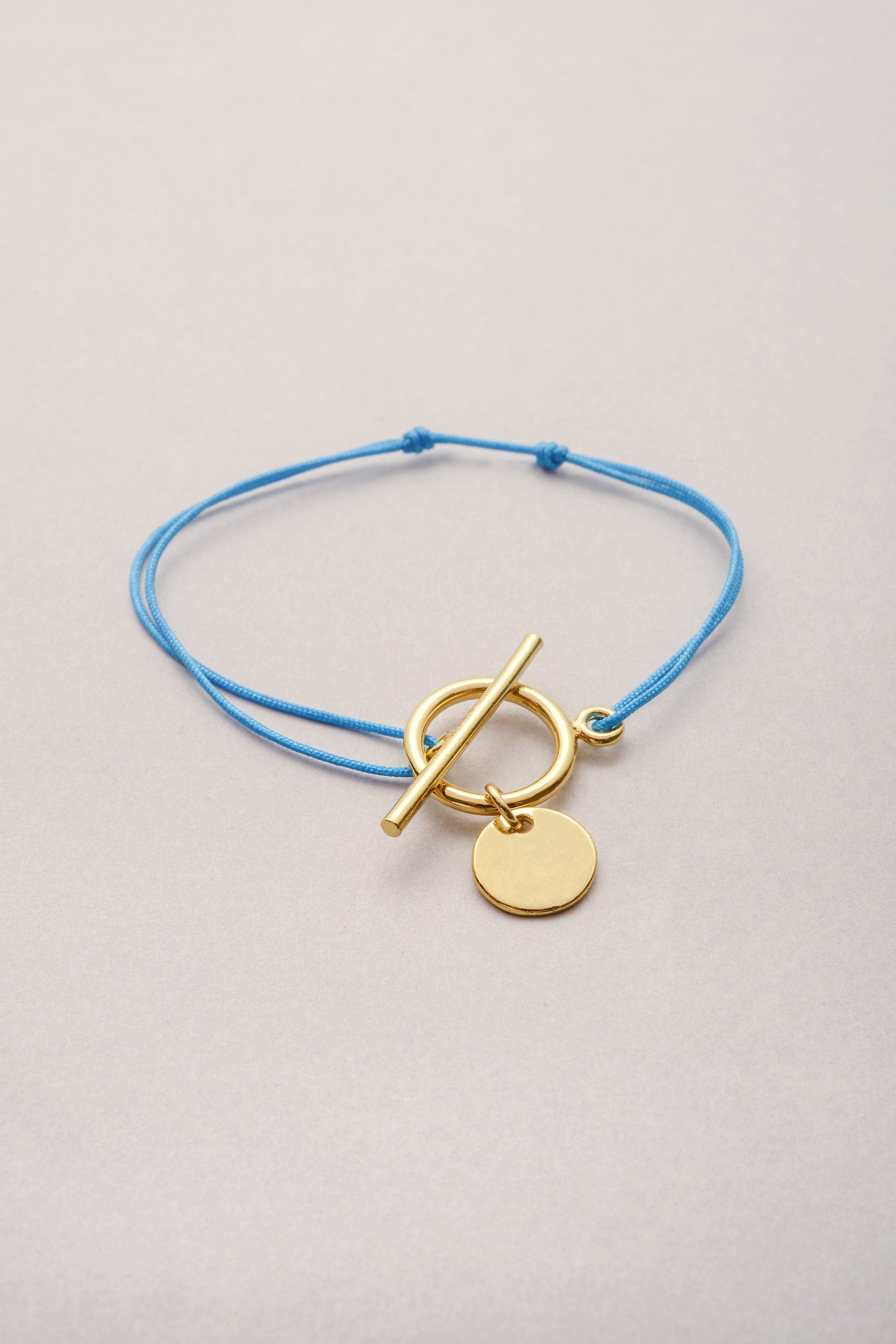 Le bracelet lou sur fil fin coloré avec son pendentif médaille doré lisse et son fermoir en T