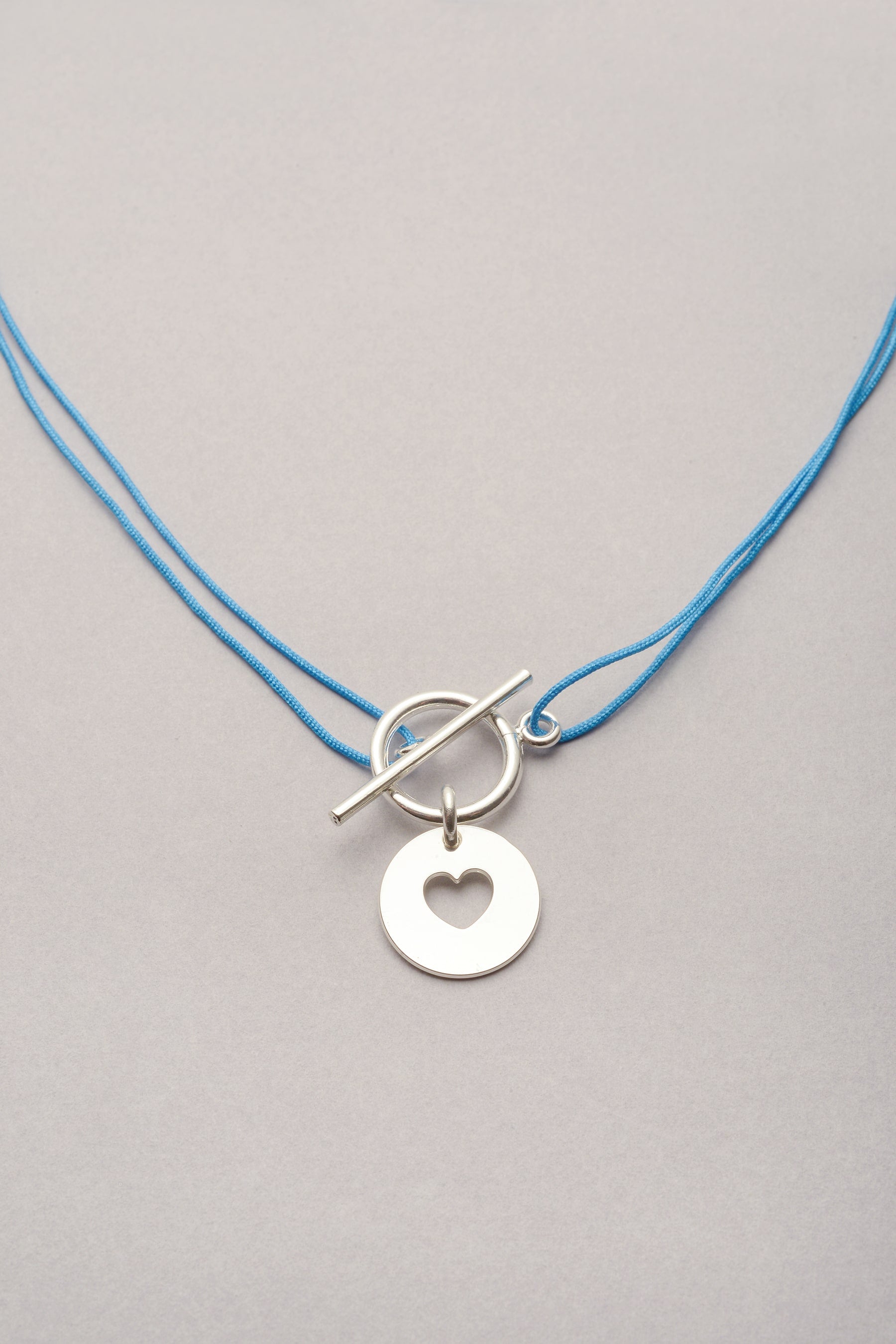 Le collier Musardise avec son coeur argenté ajouré est réglable grâce à son cordon coloré personnalisable