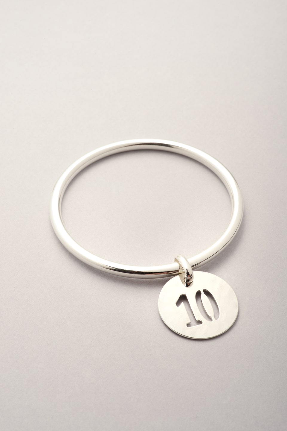 Ce bijou est composé d'un jonc argenté et d'une médaille avec un chiffre évidé. Bijou fantaisie pour femme argenté. 