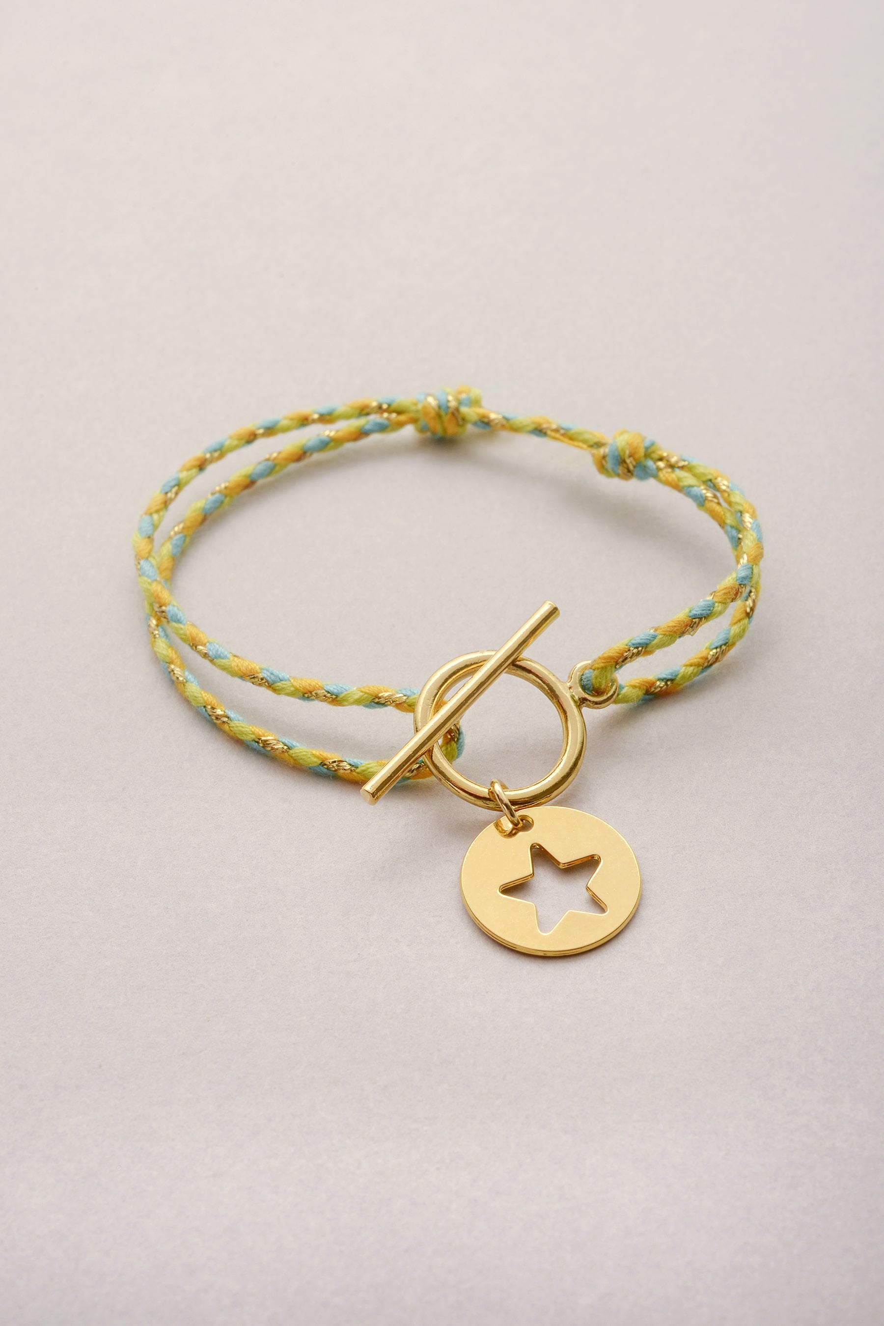 Bracelet en cordon tressé coloré avec sa pampille dorée en forme d'étoile ajouré et son fermoir en T.