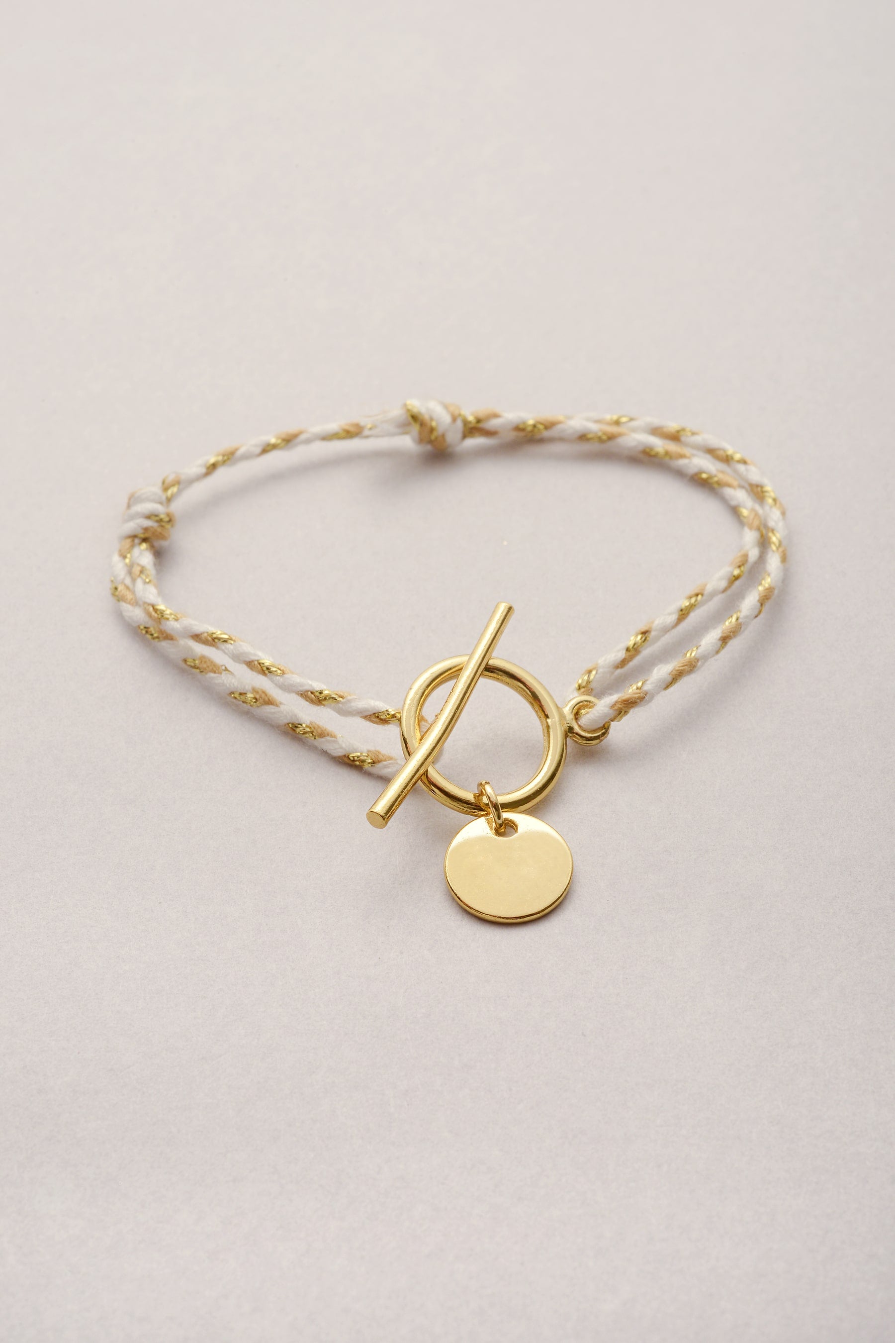 Bracelet en cordon tressé coloré avec sa pampille dorée en forme de coeur ajouré et son fermoir en T.
